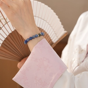 Detail of blue beaded bracelet with silver flower spacers worn against a silk fan