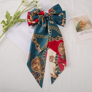 Detailed close-up of dark green and red satin hair bow clip with gold chain print patterns