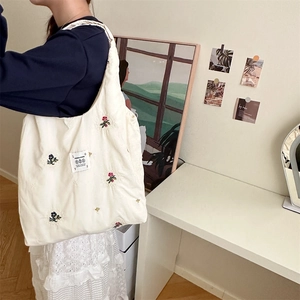 Detail of floral embroidery on cream canvas tote bag worn on shoulder in indoor setting