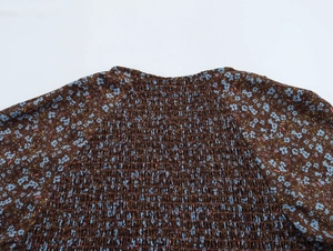 Close-up of smocking detail on a floral chiffon dress with a dark brown base and blue flowers