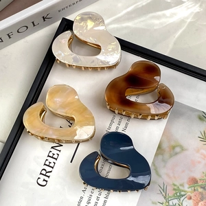 Irregular acetate claw clips in white, amber, blue, and beige with gold metal grips