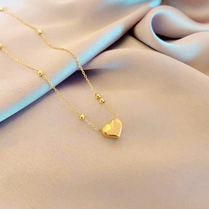Detail view of a golden heart pendant necklace with small beads on soft purple silk