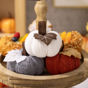 Three knitted decorative pumpkins in orange, white and gray on a wooden tiered tray