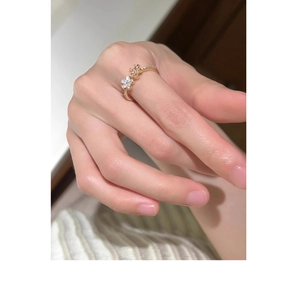 Detailed close-up of a gold floral ring with pearls and tiny diamonds on a finger
