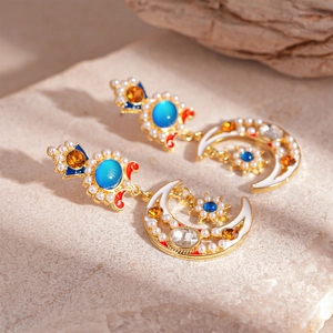 Macro shot of gold moon and star earrings with blue stones and pearls on stone surface