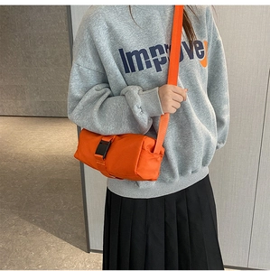 Detail view of the orange cylinder crossbody bag with black plastic buckle and adjustable strap