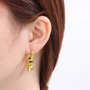 Detailed view of 18K gold-plated bamboo-style hoop earrings worn by a model