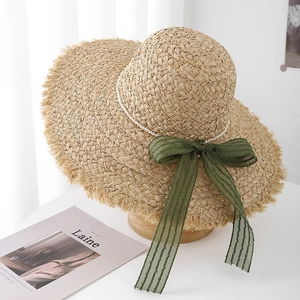 Dettaglio cappello di paglia a tesa larga con bordi sfrangiati, perle e fiocco verde