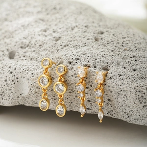 Close-up of 18K gold earrings with cubic zirconia set on a textured grey stone