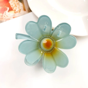 Detail of blue plumeria hair claw clip with orange gradient center on a white plate
