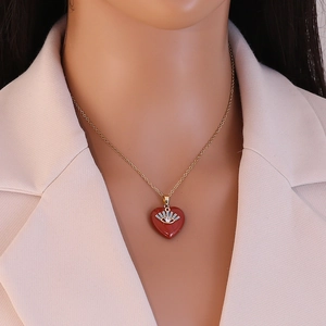 Detail of red heart pendant necklace with gold evil eye motif on a beige blazer model