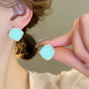 Gros plan de boucles d'oreilles carrées argentées avec glaçage vert menthe sur l'oreille