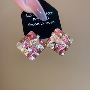Macro shot of rhombus gold earrings with pink and beige enamel and cubic zirconia detail