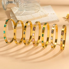 Close-up of golden bangle bracelets set with colorful rectangular stones on stone tray