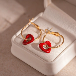Detail of gold heart earrings with red enamel charms on soft jewelry box background