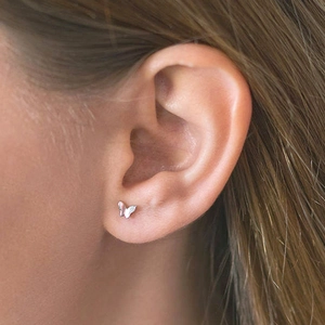 Macro close-up of a delicate silver butterfly stud earring worn by a female model