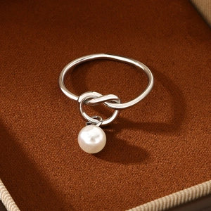 Close-up of a silver knot ring featuring a round white pearl charm in a brown jewelry box