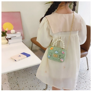 Close-up of green silicone crossbody bag with pearl handle and cartoon charms on child