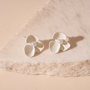 Detail of matte white flower stud earrings with central pearl on a beige stone block