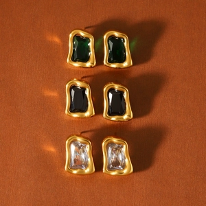 Détail de boucles d'oreilles dorées style lave avec zircons émeraude, noirs et clairs