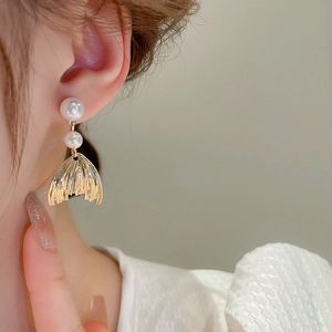 Elegant fishtail pearl earrings with golden alloy finish shown on a female model