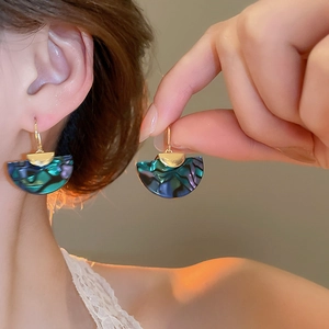 Close-up of shell fan earrings with iridescent blue-green glow on a golden hook
