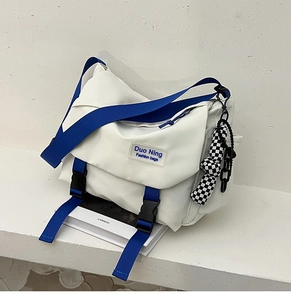 Detail view of a white nylon messenger bag with blue straps and checkered pendant on stairs