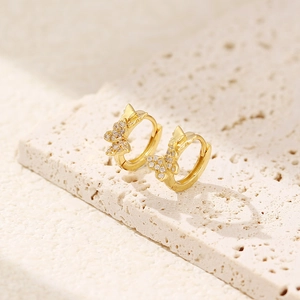 Macro shot of gold butterfly hoop earrings with sparkling crystal pavé on textured stone