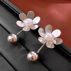 Macro detail of metallic flower petal earring with pearl and silver bead on leather