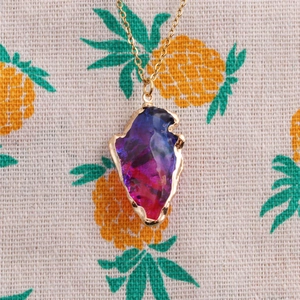 Macro detail of iridescent arrow-shaped crystal pendant with gold-plated edge and chain