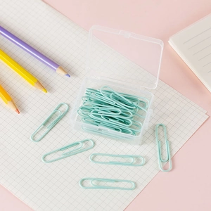 Light blue paper clips in transparent plastic box on pink desk with colorful pencils