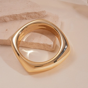 Detail of minimalist polished gold square bangle displayed on a textured stone prop