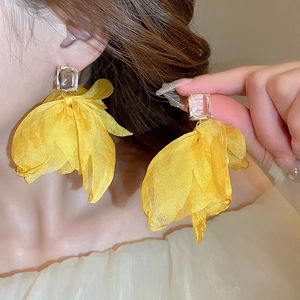 Detail view of large yellow fabric petal earrings with clear rectangular zircon stone