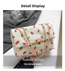 Close-up of white corduroy shoulder bag with red strawberry prints and gold chain