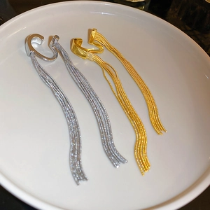 Flat lay of gold and silver metallic tassel ear cuffs with long chains on a white plate