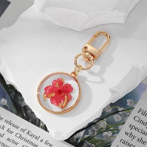 Handmade resin keychain with real red dried flowers and gold foil in a circular frame