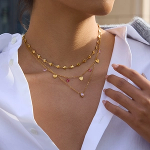 Détail de colliers superposés en or 18k avec coeurs et pendentifs zircons roses