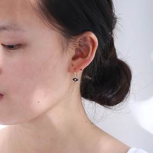 Close-up of a blue evil eye earring in gold finish worn by a model in a minimal style