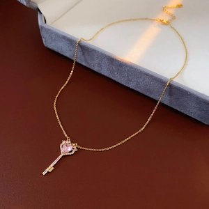 Detailed close-up of a gold key pendant with a pink heart zircon on a velvet box