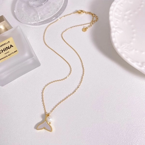 Detail of gold fish tail pendant with white shell inlay and freshwater pearl necklace