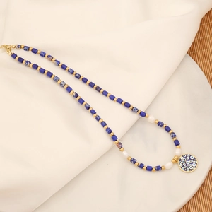 Detail of handmade natural stone necklace with blue eye pendant on a white fabric background