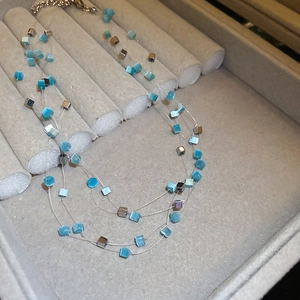 Detailed view of triple-layered beaded necklace with light blue and silver cube beads