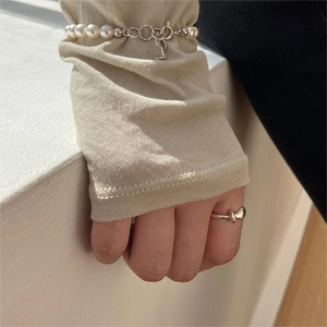 Close-up of minimalist silver knot ring and white pearl chain bracelet worn on hand