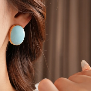 Close-up of a vintage oval turquoise earring with a gold metal border worn by a model