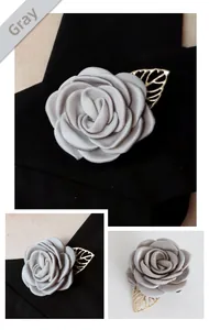Détail de la broche fleur en tissu gris avec feuille dorée ajourée sur un revers