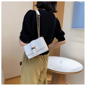 Close-up of white crocodile pattern shoulder bag with gold chain strap on a model