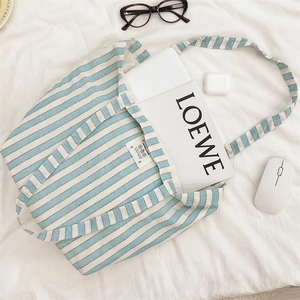 Detail of blue striped canvas tote bag with laptop and glasses on white fabric