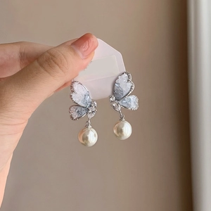 Detailed close-up of butterfly earrings with blue gradient resin wings and white pearls