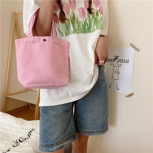 Pink canvas mini handbag with black metal snap closure shown in a lifestyle hand-held pose