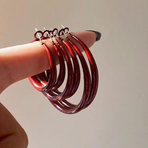 Detail showing four sizes of deep red glossy hoop earrings held by a model for comparison